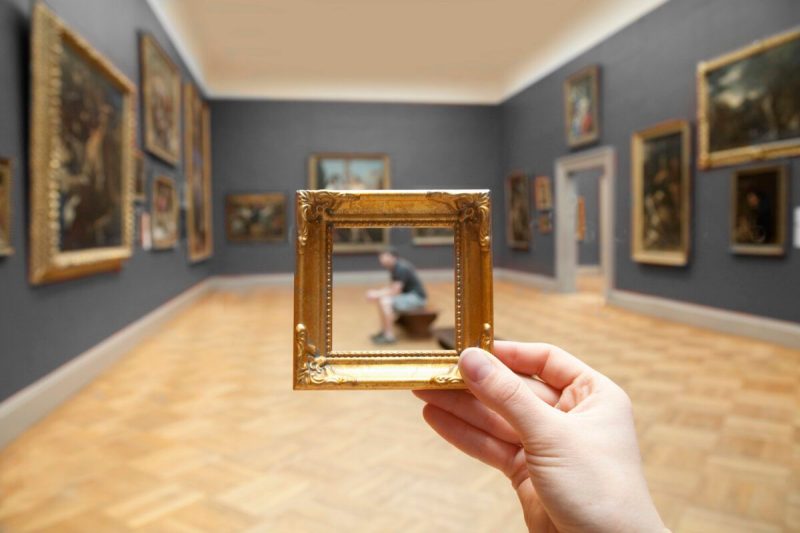 Young man sitting observing a painting framed by golden frame at a museum. (Via Getty Images)