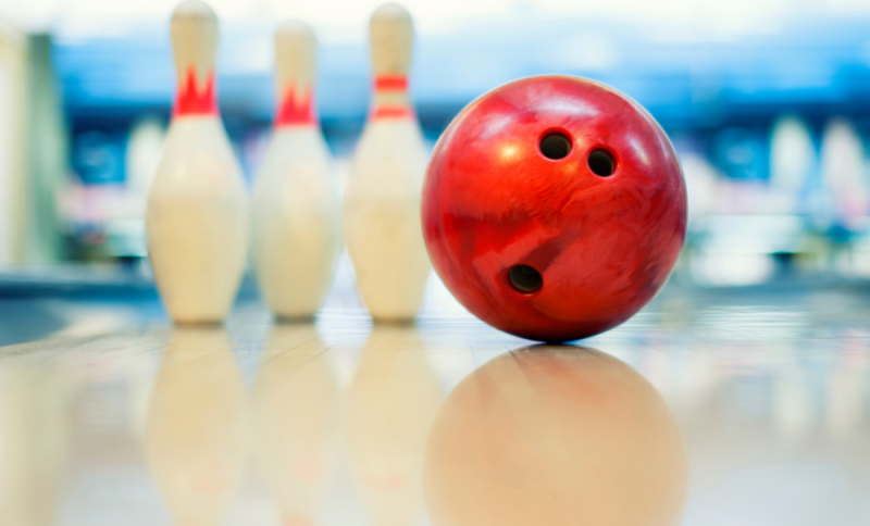 A red bowling ball and three white pins at the top of a bowling alley